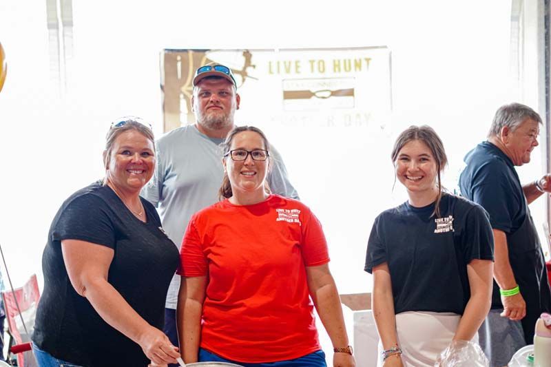 A group of people are posing for a picture in front of a sign that says `` live to hunt ''.