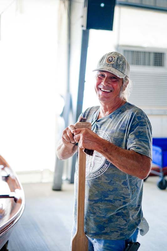 A man is holding a wooden paddle in a garage.