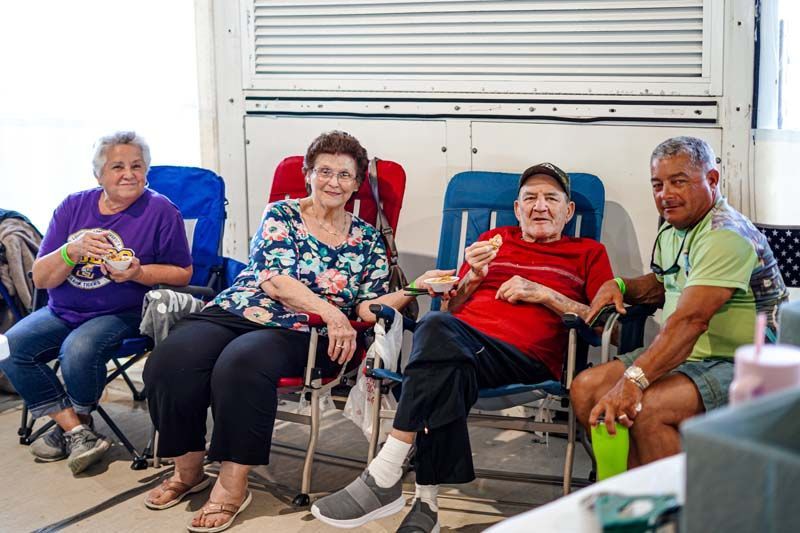 A group of elderly people are sitting in folding chairs eating ice cream.