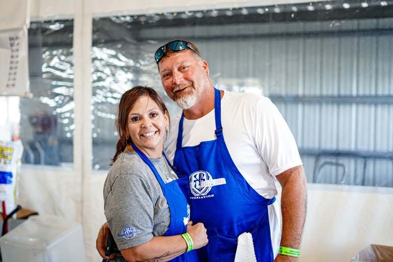 A man and a woman wearing blue aprons are posing for a picture.
