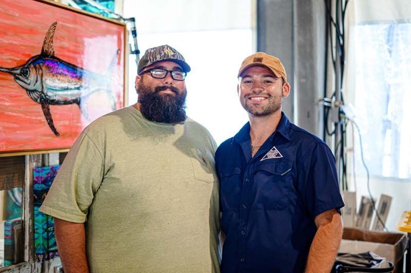 Two men are standing next to each other in front of a painting of a fish.