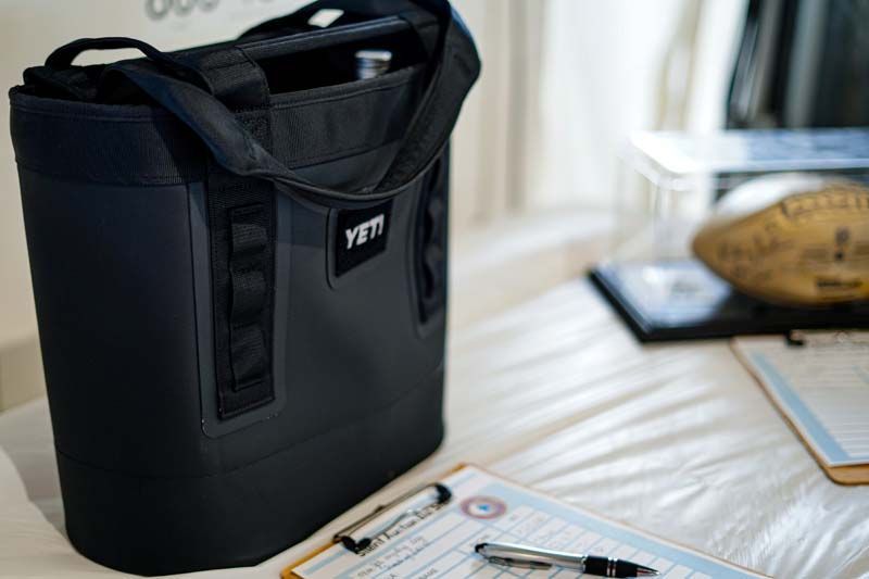 A black yeti bag is sitting on top of a clipboard on a bed.
