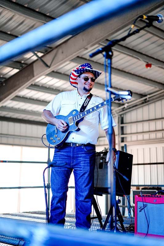 A man in a patriotic hat is playing a guitar in front of a microphone.