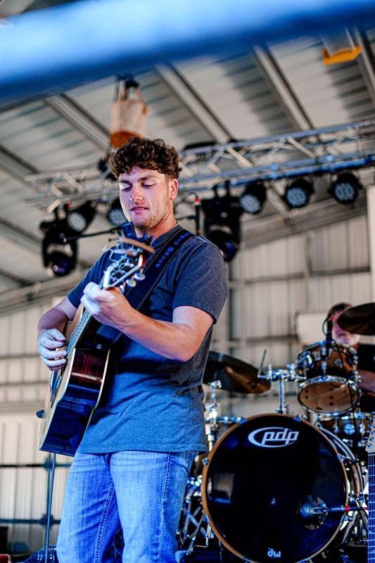 A man is playing a guitar on stage in front of a drum set.