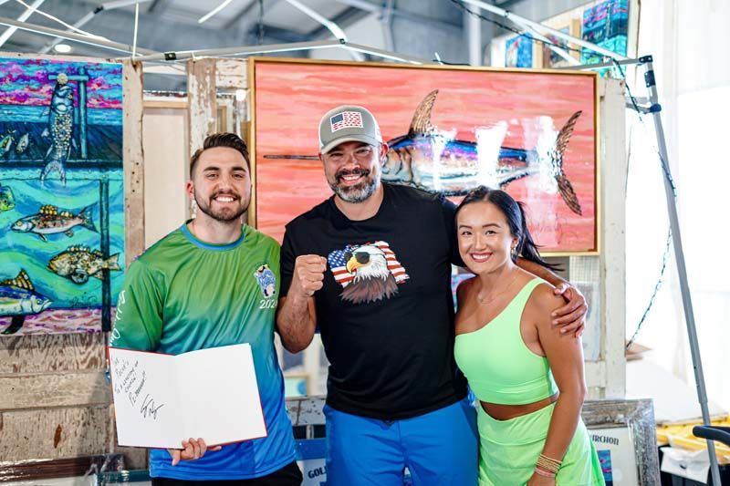 A man and two women are posing for a picture in front of a painting.