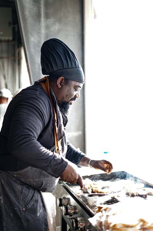 A man in a chef 's hat is cooking food on a grill.