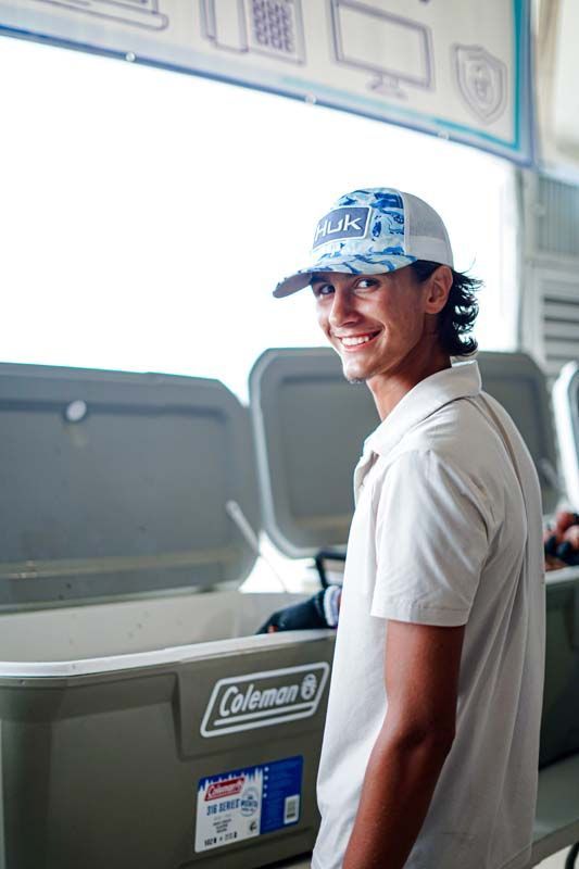 A man wearing a hat is standing next to a coleman cooler
