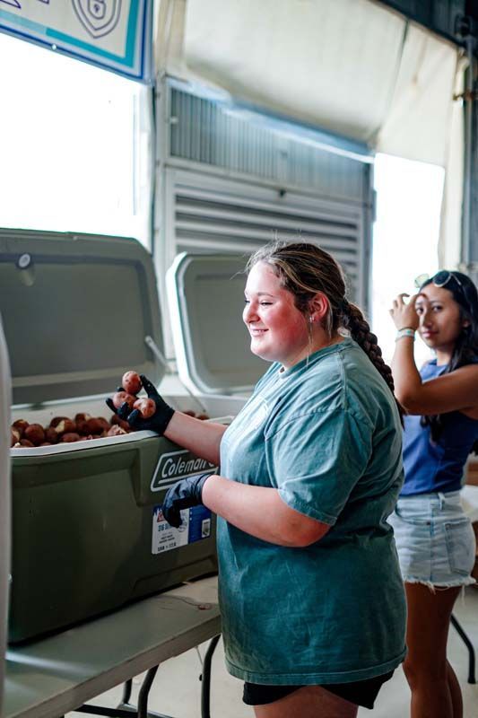 A woman is standing next to a cooler filled with food.