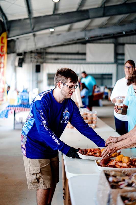 A man in a blue shirt is serving food to people at a table.
