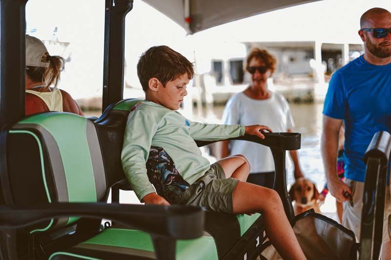 A young boy is sitting in the back seat of a golf cart.