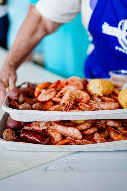 A person is holding a tray of shrimp , corn , and sausage.