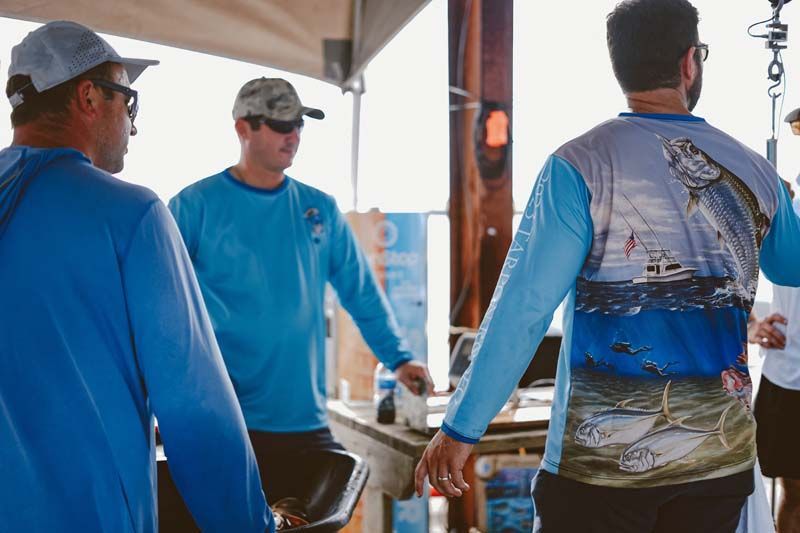 A group of men wearing blue shirts with a fish on the back are standing next to each other.