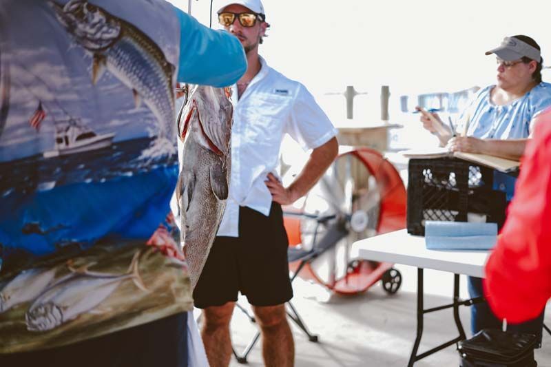A man is holding a large fish in his hand while standing next to a table.