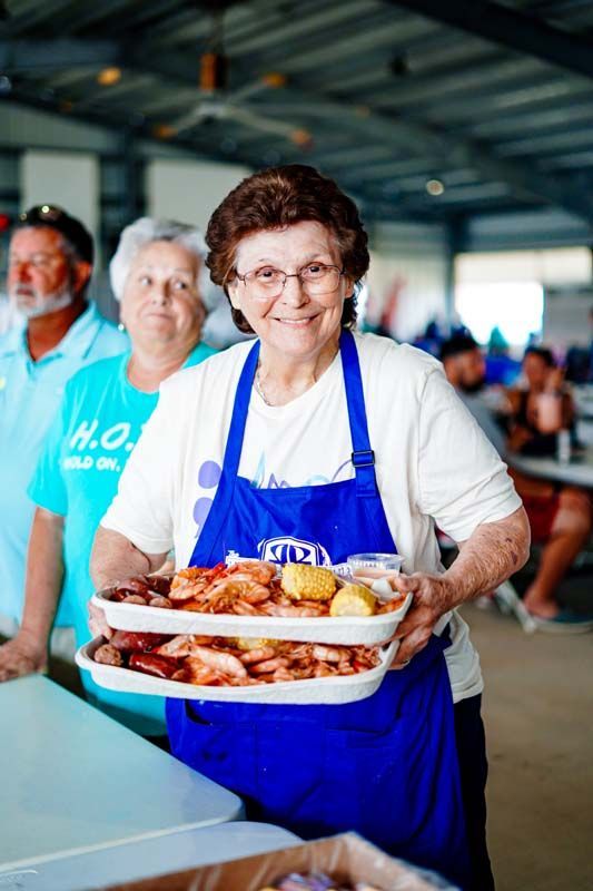 A woman in a blue apron is holding a tray of food.
