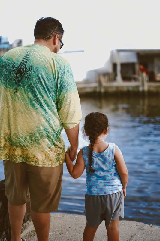 A man and a little girl are holding hands and looking at the water.