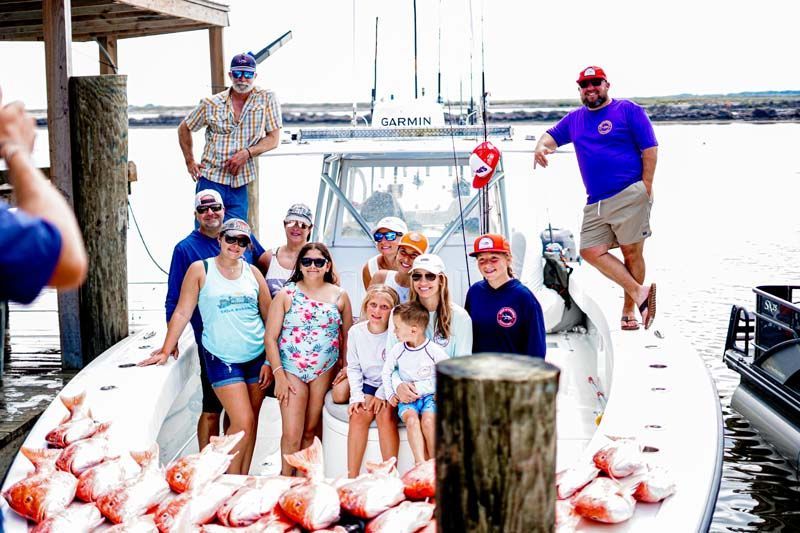 A group of people are posing for a picture on a boat filled with fish.