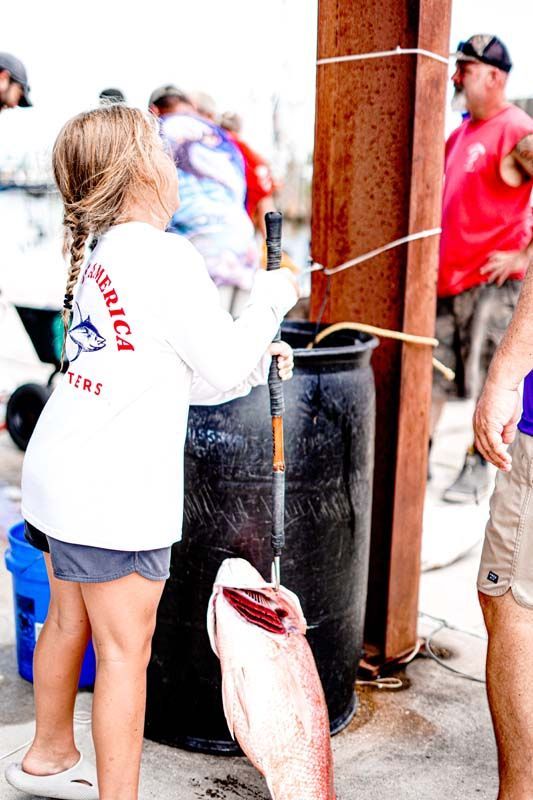 A little girl is standing next to a large fish with a fishing rod in her hand.
