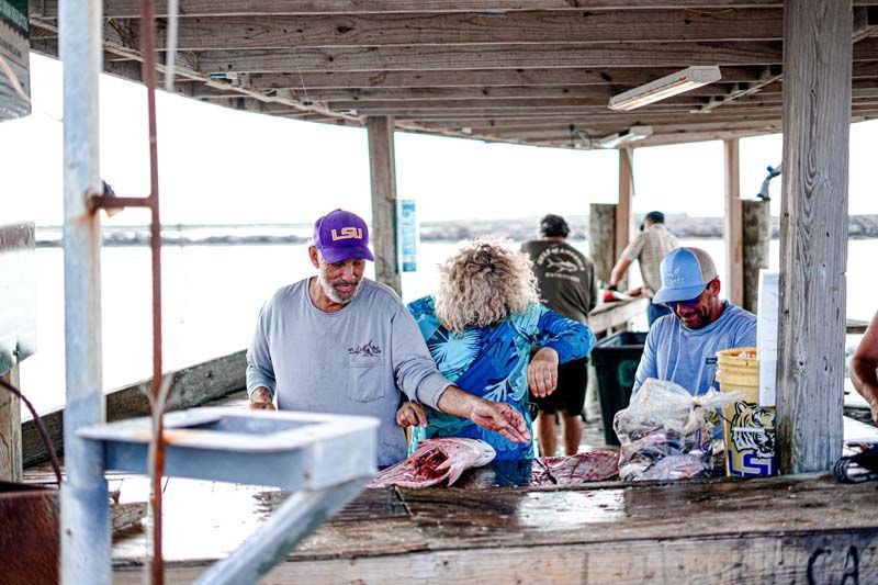 A group of people are standing around a table selling fish.