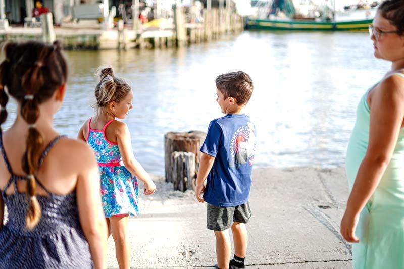 A group of children are standing on a dock looking at the water.