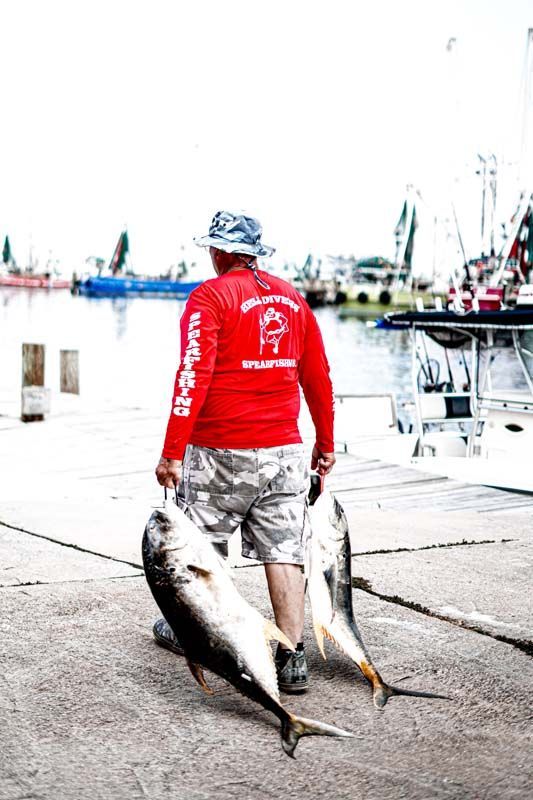 A man in a red shirt is carrying two large fish
