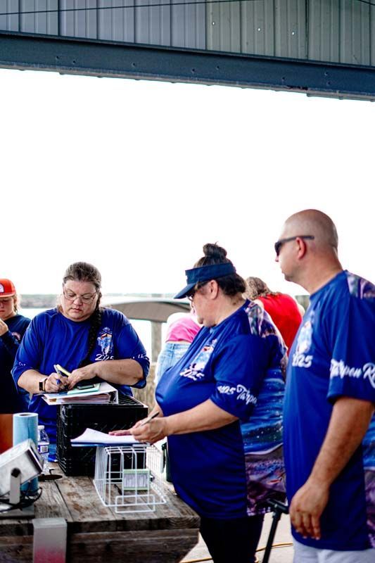 A group of people in blue shirts are standing around a picnic table.