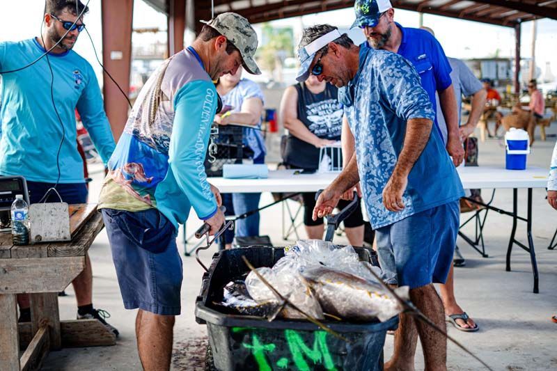 A group of men are standing around a bucket of fish.