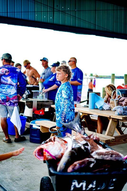 A woman is standing next to a wheelbarrow full of fish.