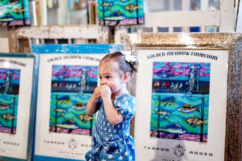 A little girl in a blue dress is standing in front of a painting.