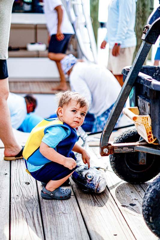 A little boy is squatting on a wooden deck next to a wagon.