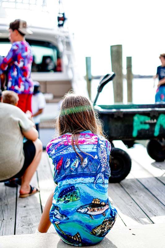 A little girl is sitting on a dock looking at a boat.