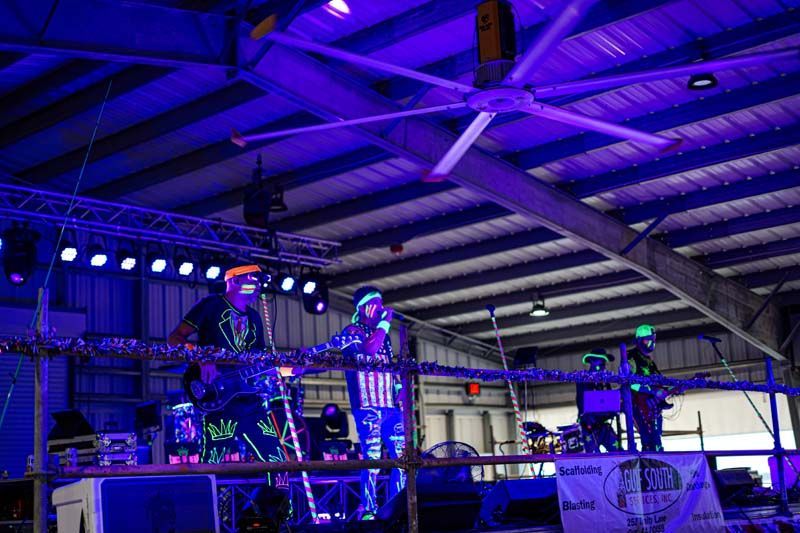 A man is standing on a stage in a large building with a ceiling fan.