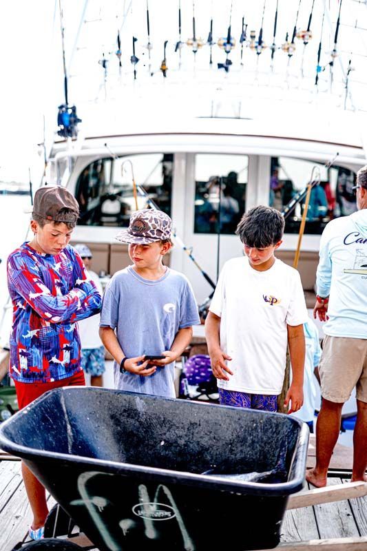 A group of young boys are standing next to a wheelbarrow on a dock.