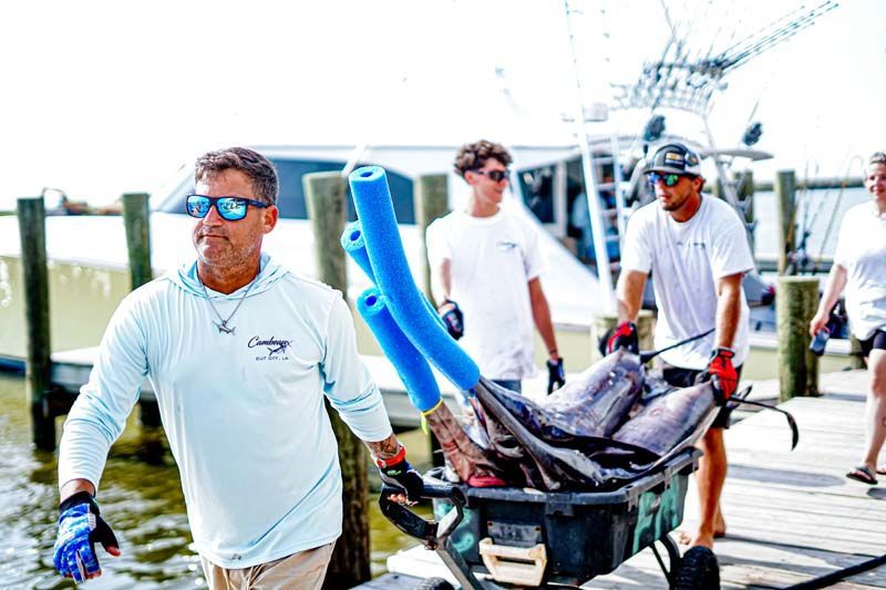 A man is pushing a wheelbarrow full of fish to a boat.