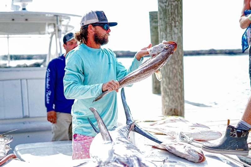 A man is holding a fish over a table.
