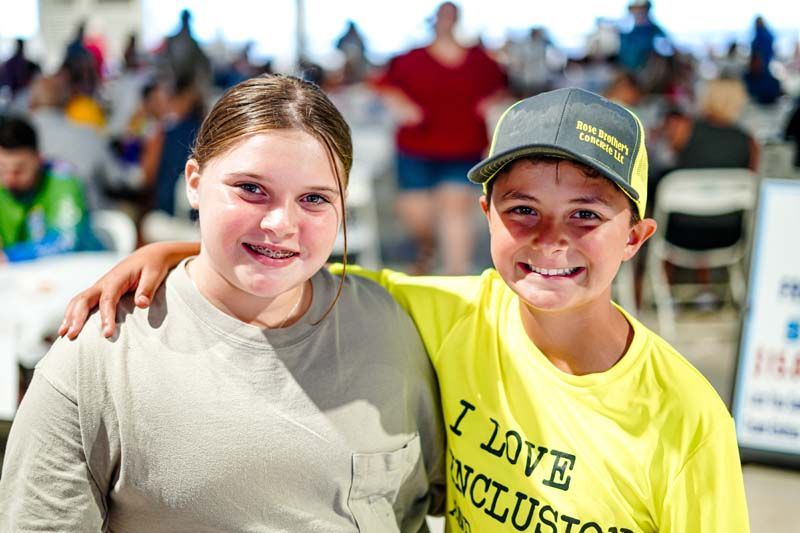 A boy and a girl are posing for a picture and the boy is wearing a yellow shirt that says i love inclusion.