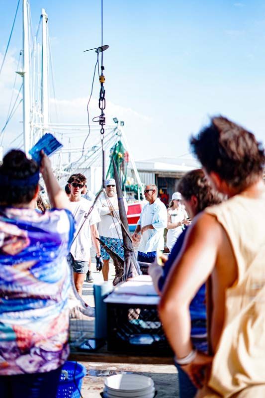 A group of people are standing around a boat with a large fish hanging from the side.