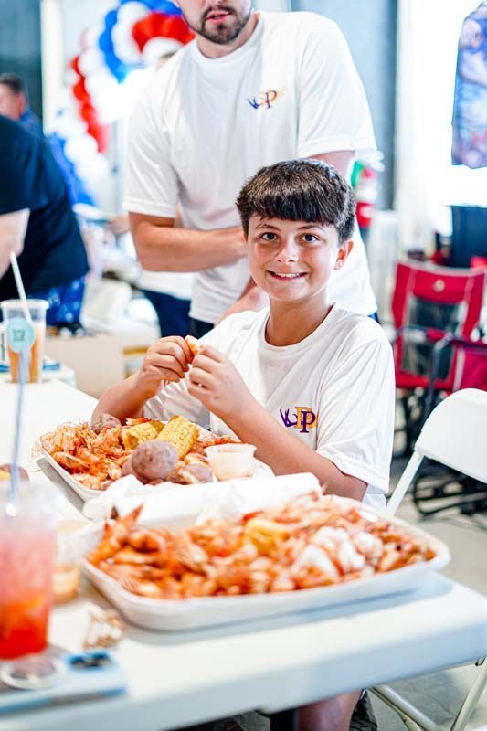 A young boy is sitting at a table eating shrimp.