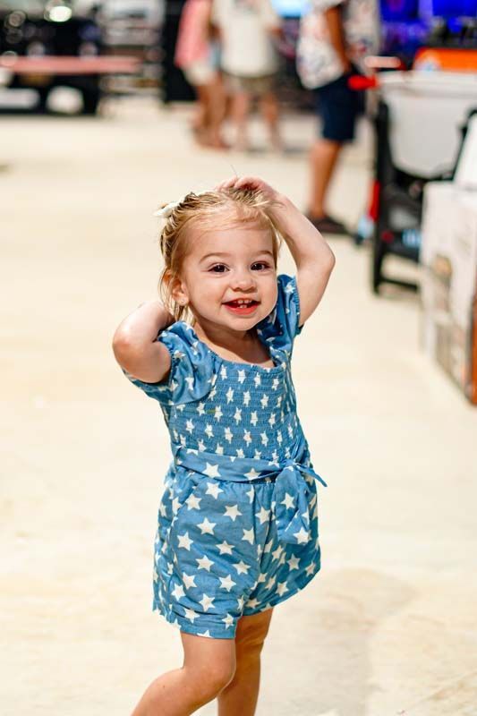 A little girl in a blue dress is standing on a white floor.