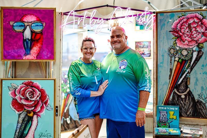A man and a woman are standing next to each other in front of paintings.