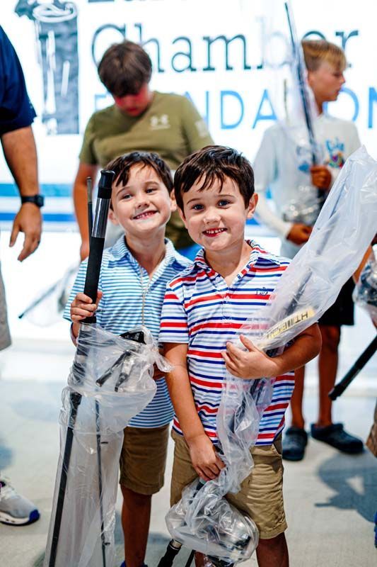 Two young boys are standing next to each other holding golf clubs.