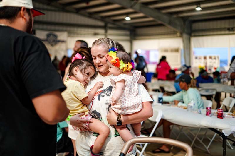 A woman is holding two babies in her arms in a crowded room.