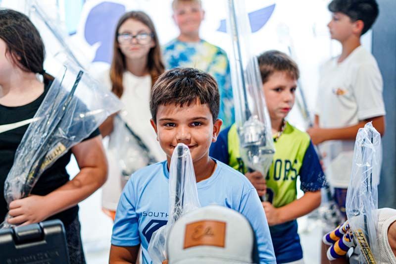 A group of children are standing next to each other holding fishing rods.