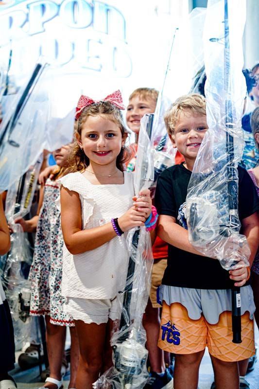 A group of children are holding fishing rods wrapped in plastic.