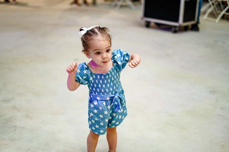A little girl in a blue dress is standing on the floor.