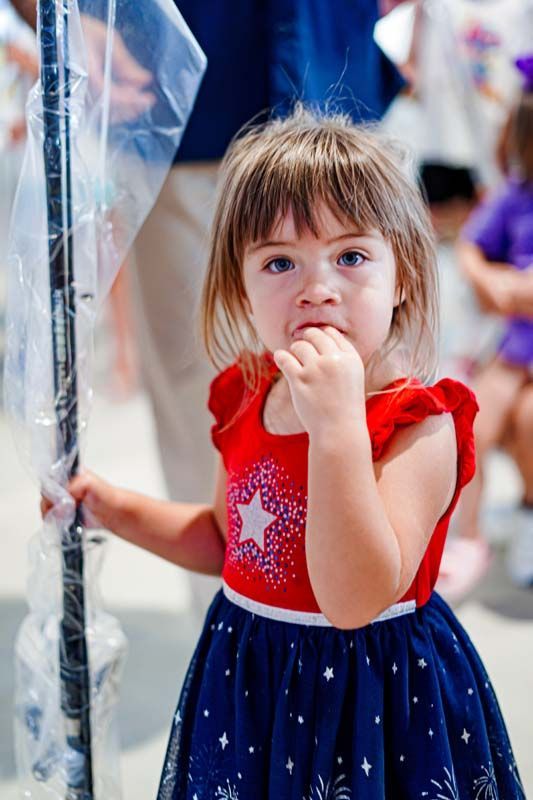 A little girl in a red and blue dress is holding a bubble wand.