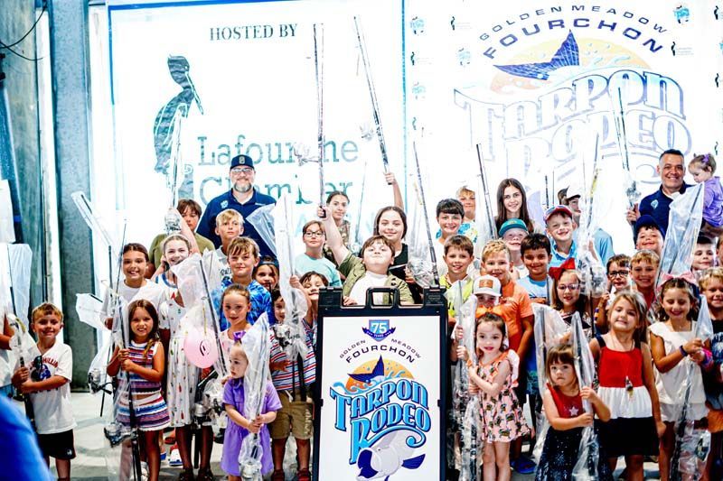 A group of children are standing in front of a sign holding fishing rods.