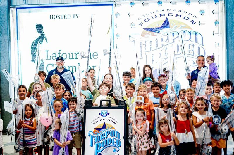 A large group of people are standing in front of a sign holding fishing rods.