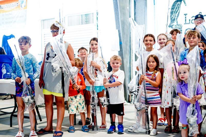 A group of children are standing next to each other holding fishing rods.