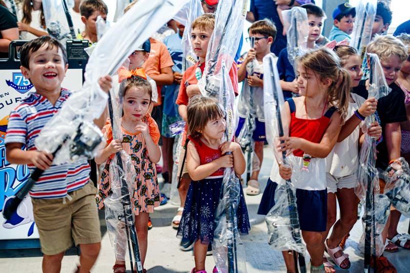 A group of children are standing in a line holding fishing rods.
