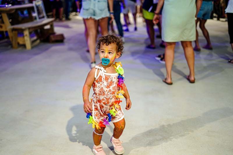 A little girl with a pacifier in her mouth is standing in a crowd of people.